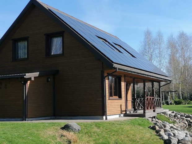 Saulės elektrinė ant tamsaus medinio namo stogo
