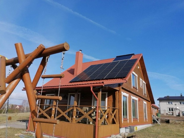 Saulės elektrinė ant medinio namo su raudonu stogu